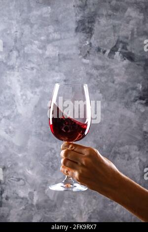 Nahaufnahme von weiblichen Armen wirbelnden Weinglas mit teuren Pinot Noir Wein in einer Hand gegen Licht grunged Betonwand Hintergrund. Zugeschnittenes Bild, CO Stockfoto