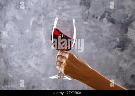 Nahaufnahme von weiblichen Armen wirbelnden Weinglas mit teuren Pinot Noir Wein in einer Hand gegen Licht grunged Betonwand Hintergrund. Zugeschnittenes Bild, CO Stockfoto