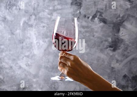 Nahaufnahme von weiblichen Armen wirbelnden Weinglas mit teuren Pinot Noir Wein in einer Hand gegen Licht grunged Betonwand Hintergrund. Zugeschnittenes Bild, CO Stockfoto