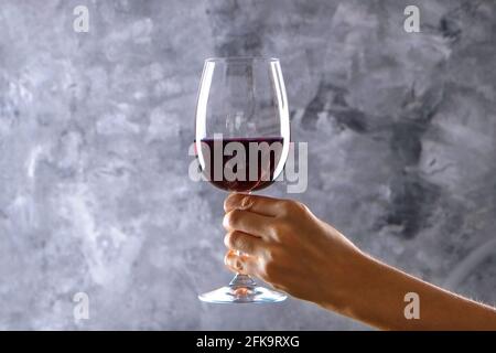 Nahaufnahme von weiblichen Armen wirbelnden Weinglas mit teuren Pinot Noir Wein in einer Hand gegen Licht grunged Betonwand Hintergrund. Zugeschnittenes Bild, CO Stockfoto