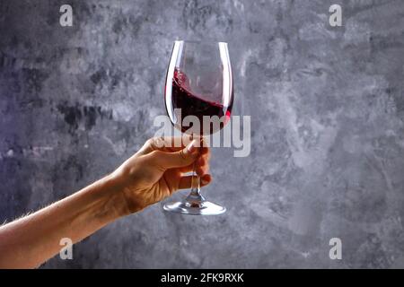 Nahaufnahme von weiblichen Armen wirbelnden Weinglas mit teuren Pinot Noir Wein in einer Hand gegen Licht grunged Betonwand Hintergrund. Zugeschnittenes Bild, CO Stockfoto