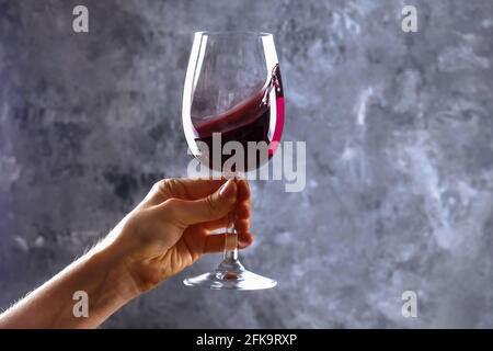 Nahaufnahme von weiblichen Armen wirbelnden Weinglas mit teuren Pinot Noir Wein in einer Hand gegen Licht grunged Betonwand Hintergrund. Zugeschnittenes Bild, CO Stockfoto