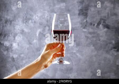 Nahaufnahme von weiblichen Armen wirbelnden Weinglas mit teuren Pinot Noir Wein in einer Hand gegen Licht grunged Betonwand Hintergrund. Zugeschnittenes Bild, CO Stockfoto