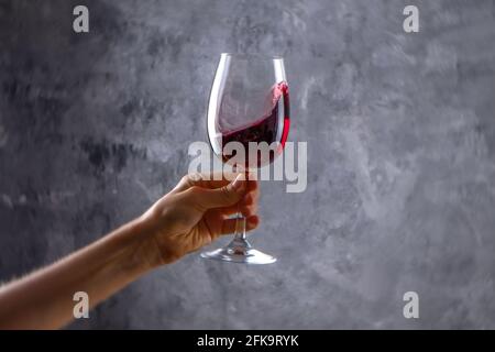 Nahaufnahme von weiblichen Armen wirbelnden Weinglas mit teuren Pinot Noir Wein in einer Hand gegen Licht grunged Betonwand Hintergrund. Zugeschnittenes Bild, CO Stockfoto