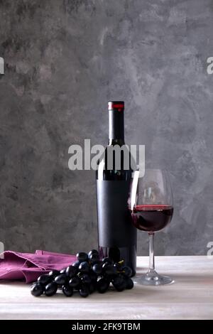 Vintage Flasche Rotwein mit leerem mattschwarzes Etikett, Trauben auf Holztisch, Betonwand Hintergrund. Teure Flasche cabernet sauvi Stockfoto