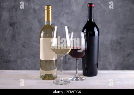 Zwei Flaschen Rot- und Weißwein mit mattem Schwarz-Weiß-Rohling auf Betonwandhintergrund. Die Weingläser sind halb voll mit teurem Wein Stockfoto