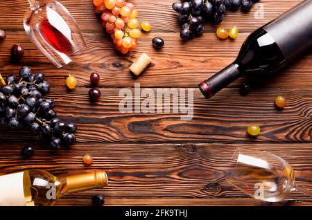 Zwei Flaschen mit Rot- und Weißwein mit blanko mattem Etikett mit Trauben verschiedener Art und Weinglas auf dunkelbraunem Holztexturtisch. Bac Stockfoto