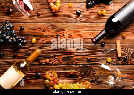 Zwei Flaschen mit Rot- und Weißwein mit blanko mattem Etikett mit Trauben verschiedener Art und Weinglas auf dunkelbraunem Holztexturtisch. Bac Stockfoto