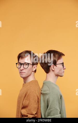 Porträt eines hübschen jungen Mannes in einer Brille, der zurücksteht Zurück mit Zwillingsbruder vor hellem Hintergrund Stockfoto