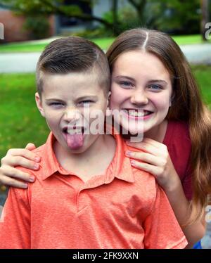 Bruder äußert seinen Ekel gegenüber Mädchen, insbesondere einer Schwester, die ihn umarmt. Er ragt aus seiner Zunge und faltet seine Nase. Schwester lächelt. Stockfoto