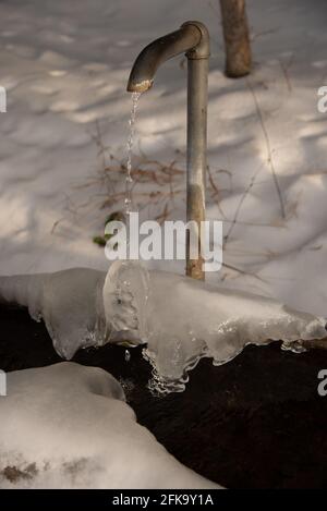 Nahaufnahme eines alten Außenwasserhahns mit dünn Fließendes Wasser in einem schneebedeckten Bereich Stockfoto