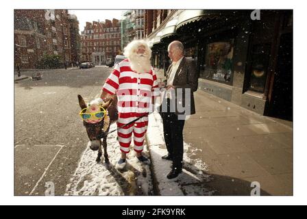 Vater Weihnachten und sein Seesel Dino posieren für Fotos vor einem schneebedeckten Harrods, bevor sie die Gäste am 9. August 2005 in London, England, im dritten Stock des Knightsbridge Stores auf eine Tour durch die Weihnachtswelt nehmen. Über 15.000ft qm Fläche sind Weihnachten im gesamten Geschäft gewidmet. Mit einer künstlichen Schneemaschine, die gegen die Sommerwärme kämpft, kommen Pater Christmas und sein Seesel Dino vor einem schneebedeckten Eingang nach Harrods zum Start von Christmas World im Knightsbridge Store in London an. Bild David Sandison 9/8/2005 Stockfoto