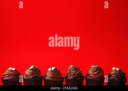 Bund von köstlichen Schokolade Buttercup Cupcakes, Zucker Herz Form Belag, isoliert auf rot. Kakaobäckerei, rustikaler Wandhintergrund, Nahaufnahme, Kopie-Spac Stockfoto