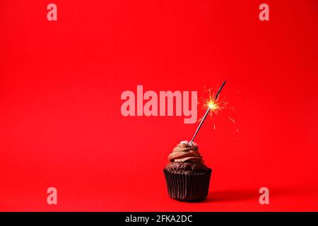 Köstliche Schokolade einzigen Butterbecher Cupcake, brennende Sprinkler Flare, bengalen Licht Feuerwerk, Zucker Belag, isoliert auf rot. Kakao Bäckerei, rustikale BA Stockfoto