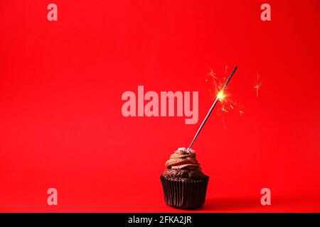 Köstliche Schokolade einzigen Butterbecher Cupcake, brennende Sprinkler Flare, bengalen Licht Feuerwerk, Zucker Belag, isoliert auf rot. Kakao Bäckerei, rustikale BA Stockfoto