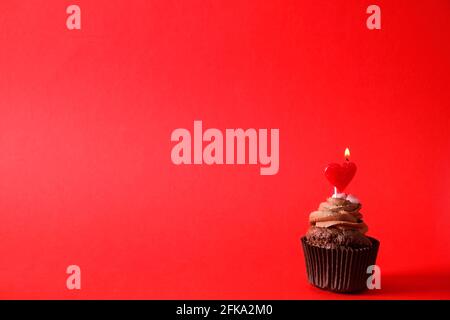 Köstliche Schokolade einzigen Butterbecher Cupcake, brennendes Herz Form festliche Kerzen, Zucker Belag, isoliert auf rot. Kakaobäckerei, rustikaler Wandhinterbau Stockfoto