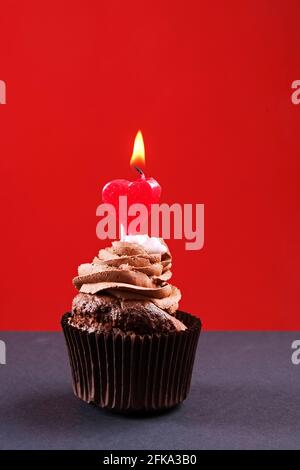 Köstliche Schokolade einzigen Butterbecher Cupcake, brennendes Herz Form festliche Kerzen, Zucker Belag, Beton Textur Tabelle. Kakaobäcker, rustikaler Kaffee Stockfoto