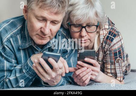 Nahaufnahme eines glücklichen Ehepaares mittleren Alters, das gemeinsam seine neuen Smartphones erkundet. Sie laden nützliche Apps herunter, tauschen Erfahrungen aus. Stockfoto