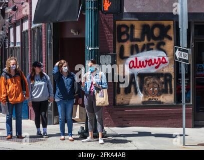 ASHEVILLE, NC, USA-25 APRIL 2021: Vier junge weiße Frauen mit COVID-Masken stehen auf der Straße neben dem Fenster mit dem Schild 'Black Lives Always Matter'. Stockfoto
