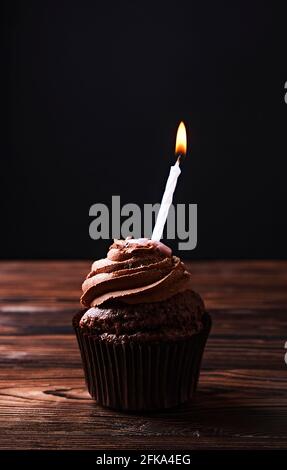 Köstliche Schokolade einzigen Butterbecher Cupcake, brennende festliche Kerzen, Zucker Belag, Holzstruktur Tabelle. Kakaobäckerei, rustikales Café Hipster t Stockfoto