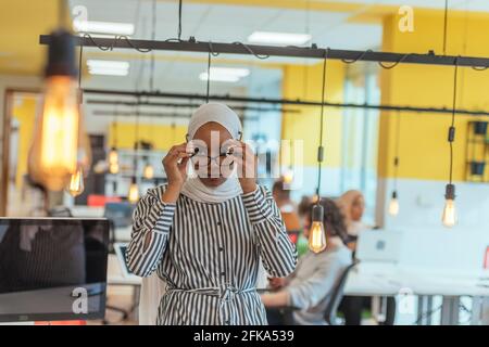 Trait einer schwarzen (afroamerikanischen) weiblichen muslimin, die in einem modernen Geschäftsbüro steht, während sie einen Hijab trägt. Stockfoto