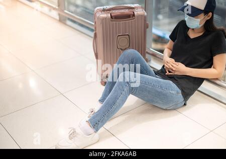 Asiatische Frau mit OP-Maske fühlt sich traurig und deprimier für verpassten oder stornierten Flug an Bord zu einem anderen Ort am Flughafen, wegen der Covid19 Stockfoto