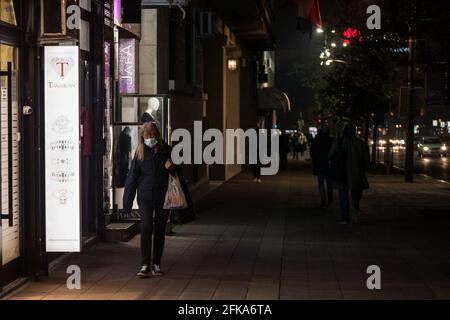 Bild einer weißen kaukasischen Frau, die nachts in Belgrad, Serbien, neben den Geschäften läuft. Sie trägt eine schützende Gesichtsmaske während der Coronavirus-Kov von 2020 Stockfoto