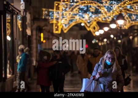 Bild einer weißen kaukasischen Frau, die nachts in Belgrad, Serbien, neben den Geschäften läuft. Sie trägt eine schützende Gesichtsmaske während der Coronavirus-Kov von 2020 Stockfoto