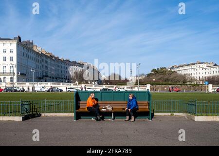 Zwei Frauen unterhalten sich auf EINER Bank an der Küste von Hove, Brighton, East Sussex, Großbritannien. Stockfoto