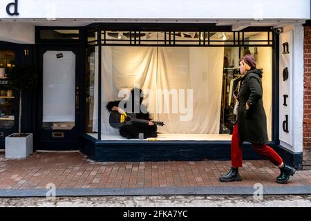 Ein Mann in EINEM Gorilla-Kostüm sitzt in EINEM Schaufenster und spielt Gitarre, The High Street, Lewes, East Sussex, Großbritannien. Stockfoto