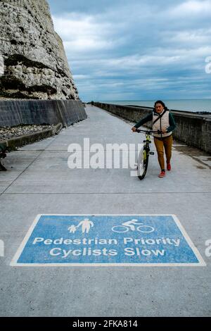 Eine Radfahrerin steigt am Undercliff Walk, Rottingdean, (nahe Brighton) East Sussex, Großbritannien, aus. Stockfoto