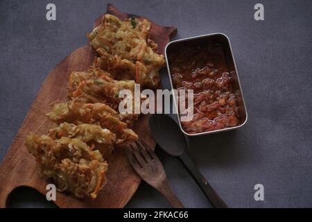 Der traditionelle Snack ist gebratener Bakwan mit Holzlöffel und Gabel auf grauem Hintergrund. Stockfoto