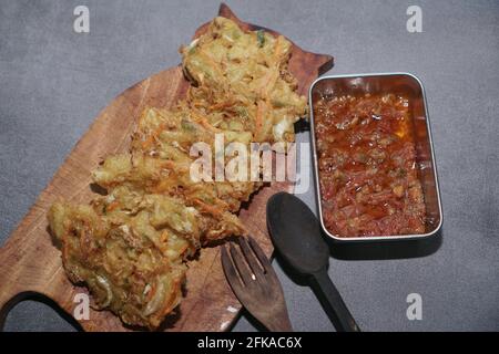 Der traditionelle Snack ist gebratener Bakwan mit Holzlöffel und Gabel auf grauem Hintergrund. Stockfoto