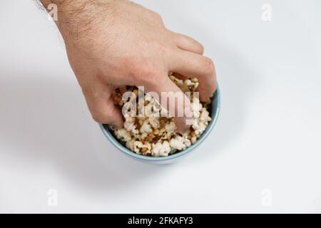 Verbrannter Popcornkern in blauer Tasse, Menschenhand nimmt Popcorn Stockfoto