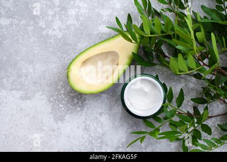 Schüssel Körpercreme mit Avocado auf grauem Hintergrund. Glas kosmetische Creme, Blätter und Avocado. Stockfoto