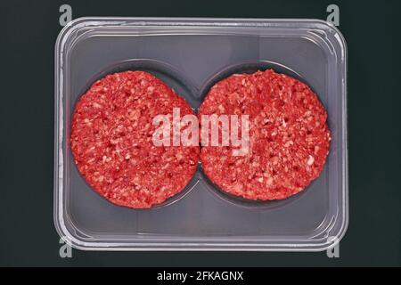 Rohe runde Burger-Patties in der Verpackung auf dunklem Hintergrund Stockfoto