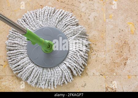 Gebrauchter runder Spinnmopp mit Mikrofaserkopf, grüner Griff auf gelbem Granit-Fliesenboden mit Copyspace Stockfoto