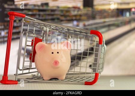 Pink Piggy Bank Schwein stehend in Mini-Shopping-Push-Cart Mit verschwommenem Supermarkthintergrund Stockfoto