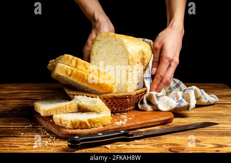 Weibliche Hände servieren frisches, hausgemachtes weißes Brot in einem Korb auf einem Holztisch. Hausgemachte Kuchen, Gebäck. Stockfoto