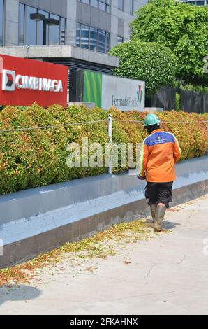 Senayan, Jakarta, Indonesien - 23. April 2021: Ein Offizier in Orange schneidet Anlagen vor den Gebäuden der CIMB Niaga und der Permata Bank. Stockfoto