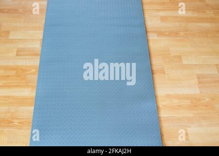 Dicke Anti Rutsch blaue Fitness Yoga Praxis oder Meditation Matte Aus PVC auf gelbem Laminat-Holzboden Stockfoto
