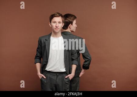Porträt des Inhalts junger Mann in grauem Anzug stehend mit Zwillingsbruder vor braunem Hintergrund Stockfoto