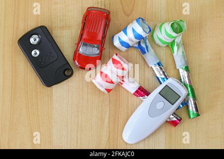 Digitales Alkoholatmtester in weiß neben einem Auto-Fernbedienung Schlüssel und bunte Party-Hörner Stockfoto