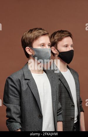 Reihe von selbstbewussten schönen jungen Zwillingen in grauen Anzügen und Stoffmasken, die in der Geschäftswelt arbeiten Stockfoto