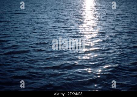 Hintergrund, blaue Weite des Ozeans Wasser am Abend Sonnenuntergang mit reflektierten Strahlen der Sonne auf den Wellen Stockfoto