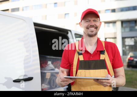 Mann Kurier in Uniform hält digitale Tablette in der Nähe des Autos Stockfoto
