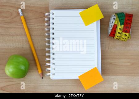 Ein leeres Notizbuch, grüner Apfel, Bleistift, Maßband auf Holzhintergrund Stockfoto