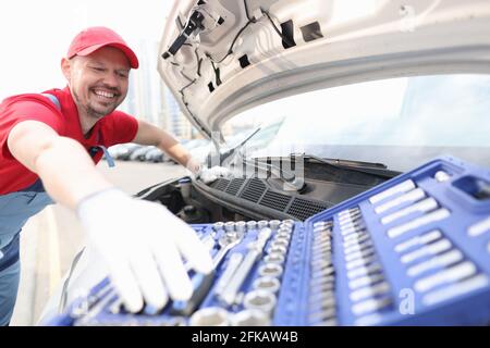 Vorarbeiter, der die Motorhaube des Autos öffnet und das Metallwerkzeug aus dem Fahrzeug nimmt Koffer Stockfoto