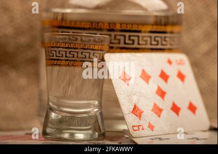 Spielkarten, ein Glas Wodka und ein Dekanter Wodka auf einem Tisch, der mit grobem Sackleinen bedeckt ist. Nahaufnahme, selektiver Fokus. Stockfoto