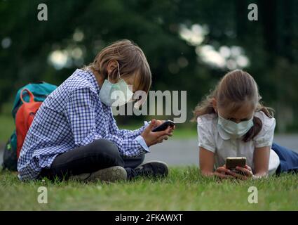 Nette Schüler mit Smartphones an der Grundschule. Junge und Mädchen in Sicherheitsmasken mit Gadgets in den Händen. Stockfoto